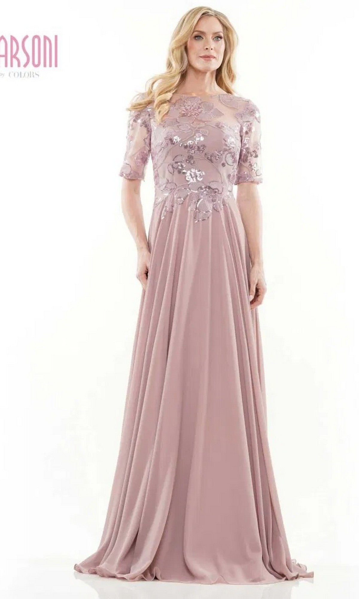 A woman wears the Marsoni M286 long formal dress in mauve, featuring a sheer sequin lace bodice and short sleeves, standing gracefully against a plain white background.
